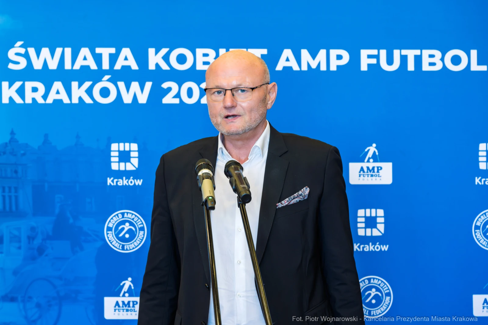 Mężczyzna przemawia przy mikrofonach na tle niebieskiego banera z logo AMP Futbol.  Autor: Piotr Wojnarowski