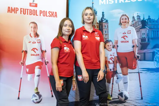 Dwie kobiety w koszulkach reprezentacyjnych, obok plakaty związane z futbolem.