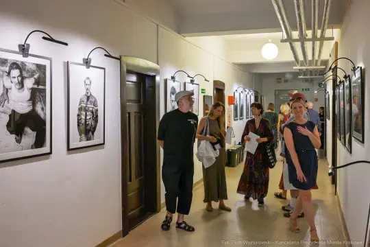 Grupa ludzi zwiedzająca wystawę zdjęć w korytarzu.