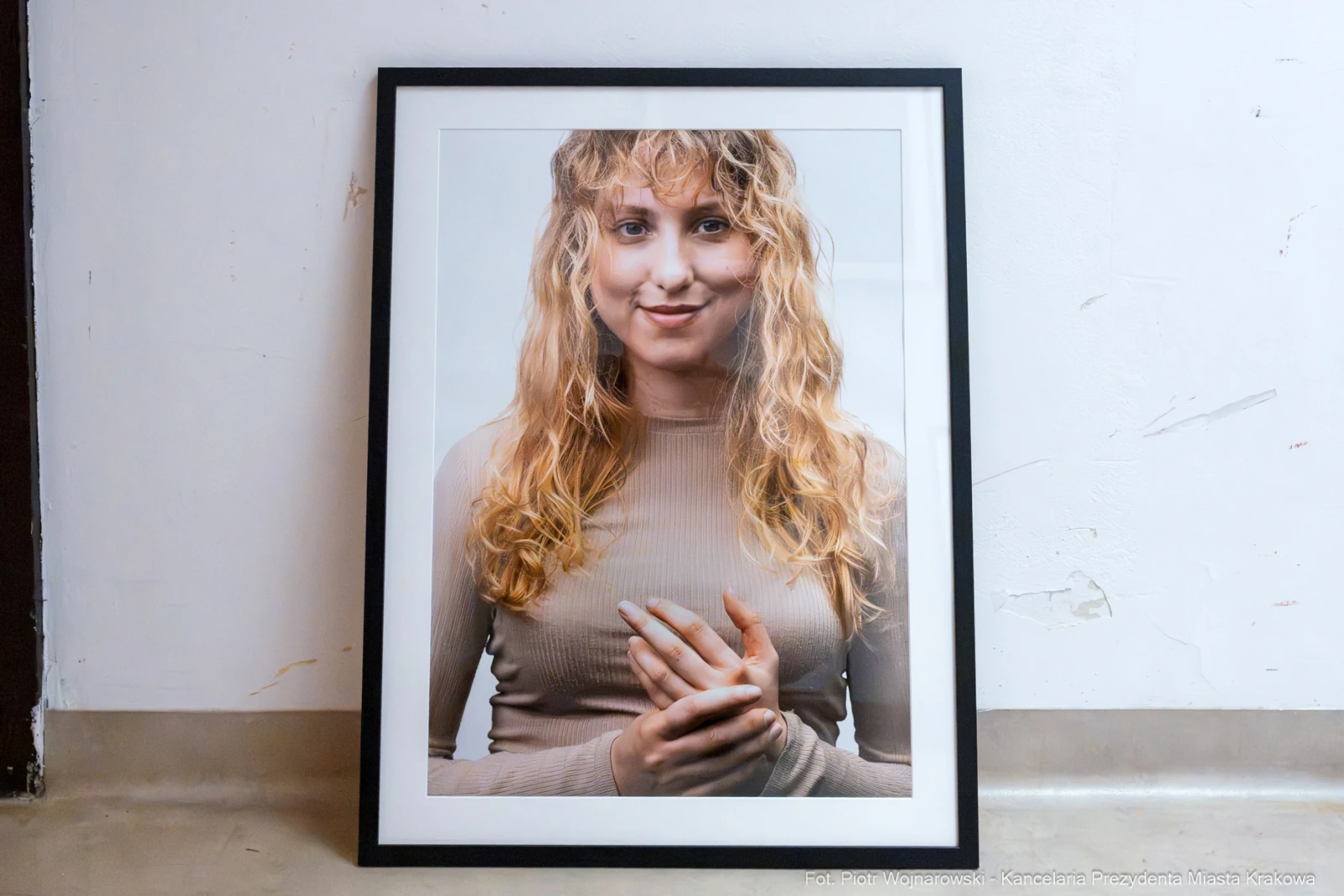 Portret uśmiechniętej kobiety z długimi, falującymi włosami, trzymającej dłonie na piersi.  Autor: Piotr Wojnarowski