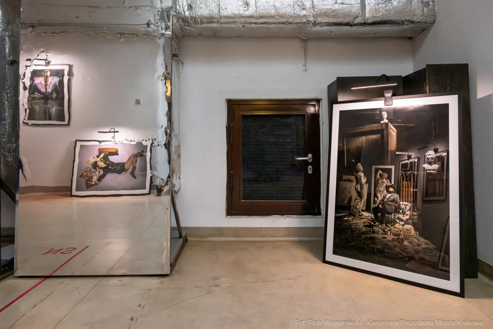 Wystawa sztuki z obrazami na ścianach i dużą ramą z dziełem na podłodze.  Autor: Piotr Wojnarowski