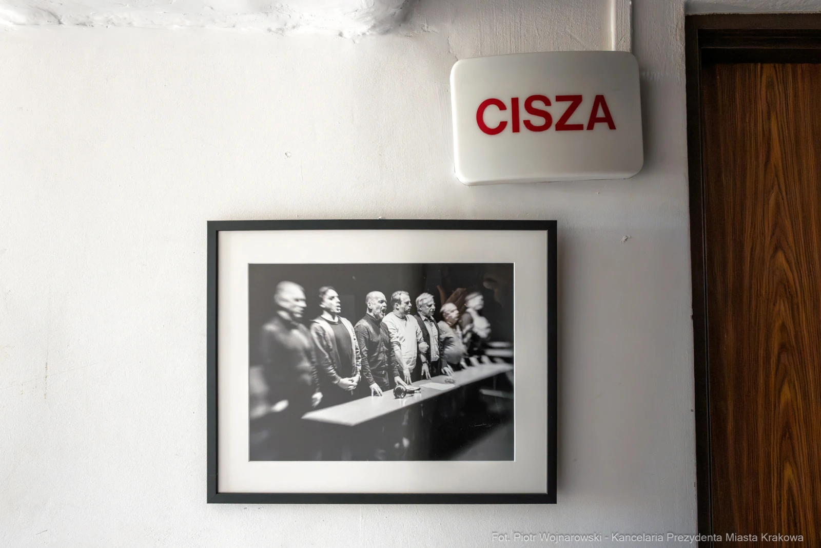 Czarnobiałe zdjęcie grupy ludzi stojących przy stole, obok napis "CISZA".  Autor: Piotr Wojnarowski
