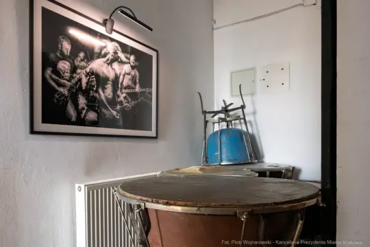 Cztery instrumenty perkusyjne w pomieszczeniu z czarno-białą fotografią muzyków na ścianie.