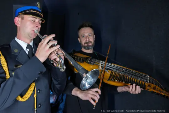 Mężczyźni grają na trąbce i instrumencie strunowym w ciemnym pomieszczeniu.