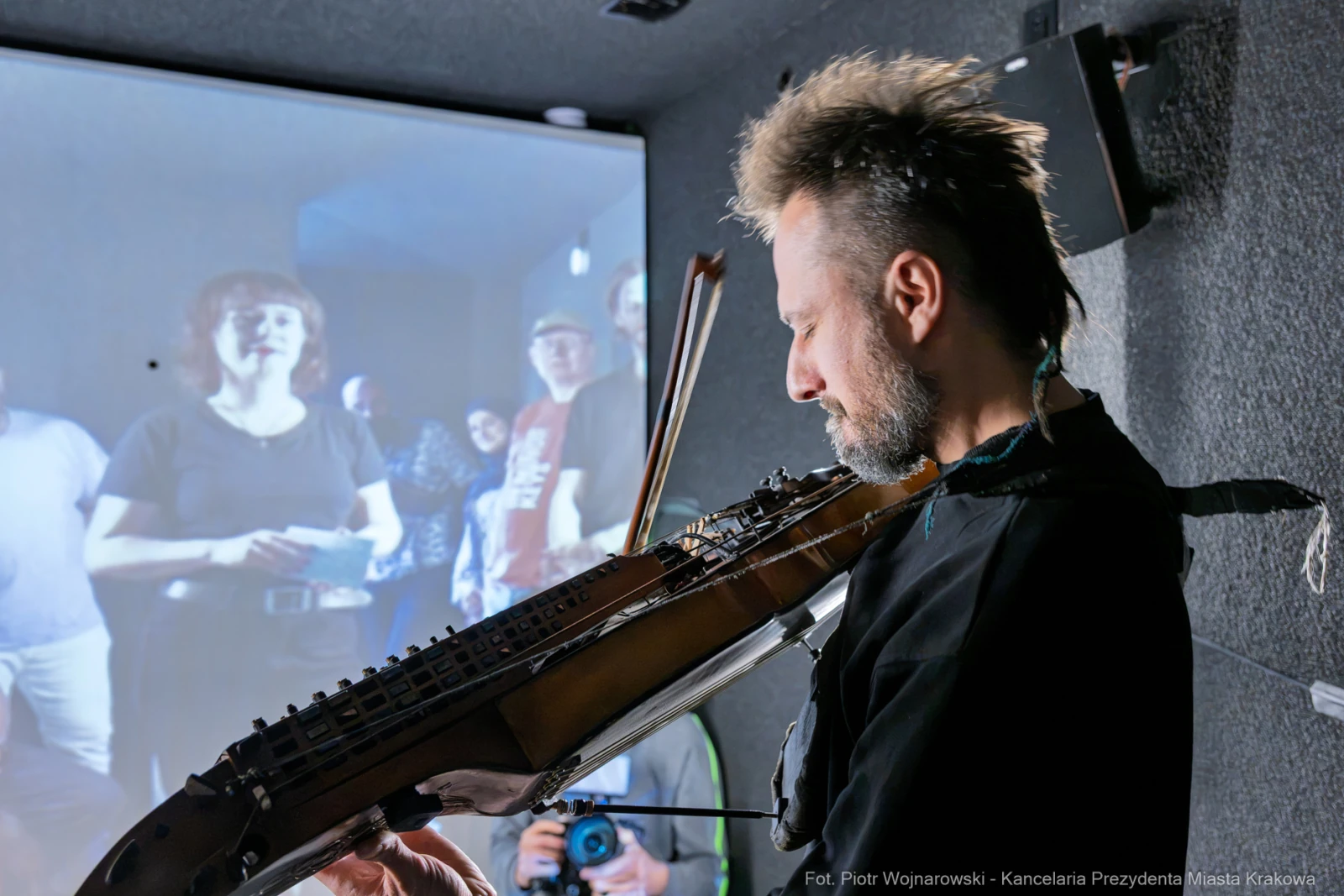 Muzyk grający na instrumentach strunowych, w tle widoczna grupa ludzi.  Autor: Piotr Wojnarowski