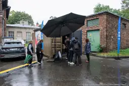 Ludzie stojący pod parasolem przy kontenerze w deszczowy dzień.