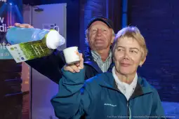 Mężczyzna nalewa napój do kubka trzymanego przez kobietę. Oboje uśmiechają się.