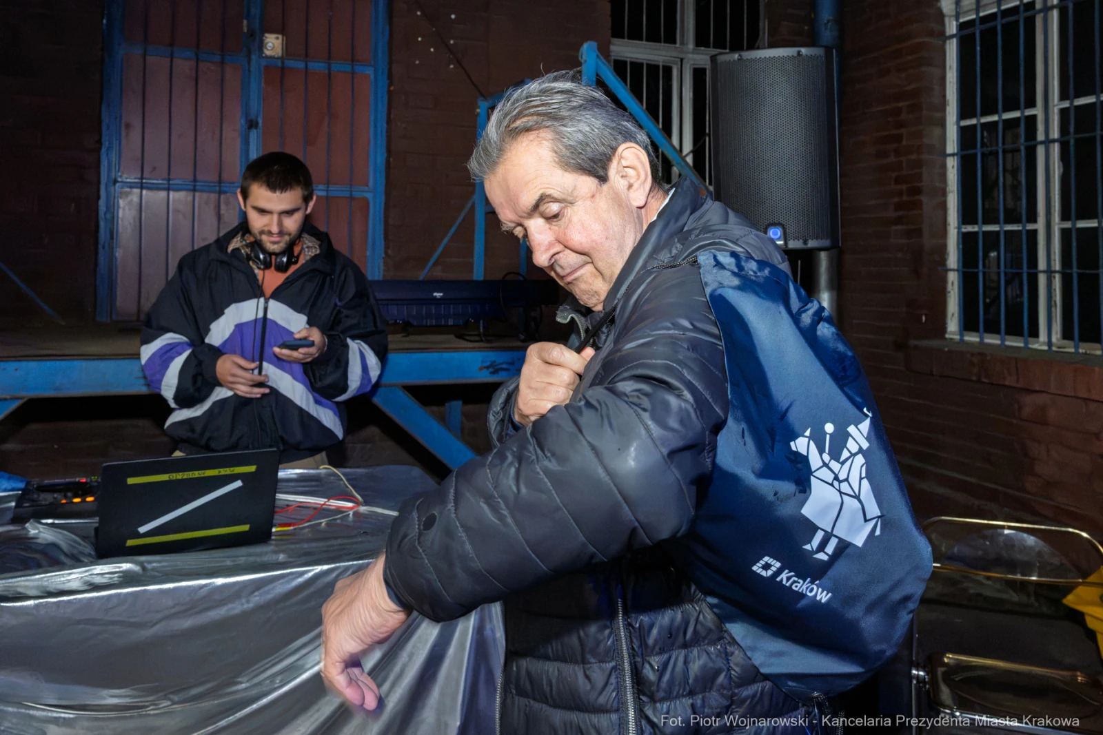 Mężczyzna z torbą na ramieniu, w tle inny mężczyzna przy laptopie.  Autor: Piotr Wojnarowski