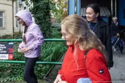 Grupa osób spacerujących w miejskim otoczeniu, jedna z nich w czerwonej kurtce.