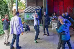 Grupa ludzi bawi się na świeżym powietrzu, niektórzy tańczą, inni rozmawiają.