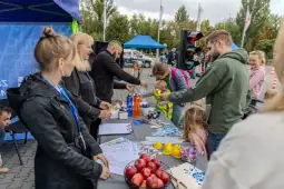 Grupa ludzi przy stoisku, rozdająca materiały promocyjne i zabawki dzieciom.