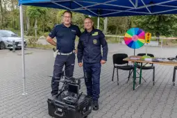 Dwóch policjantów stoi obok drona i stoiska z kołem fortuny.