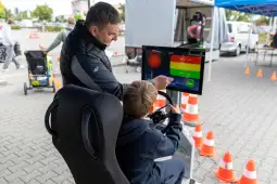 Mężczyzna pokazuje dziecku interaktywną grę na symulatorze jazdy. W tle pachołki i stoiska.