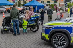 Dzieci i dorośli przy policyjnym motocyklu oraz samochodzie, w tle stoiska i namioty.