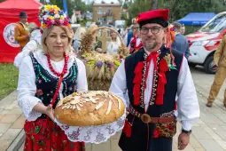 Kobieta i mężczyzna w tradycyjnych strojach ludowych trzymają chleb ozdobiony symbolami.