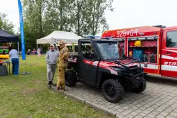 Strażak obok pojazdu terenowego, w tle wóz strażacki i namioty.