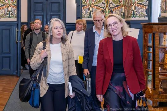 Grupa osób wchodzi do eleganckiego pomieszczenia z dekoracyjnymi ścianami.