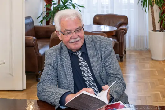 Mężczyzna w okularach przegląda książkę w eleganckim wnętrzu.