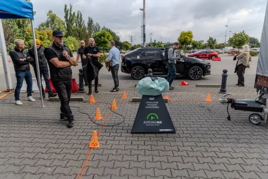 Grupa ludzi obserwuje demonstrację autonomicznego pojazdu na parkingu.