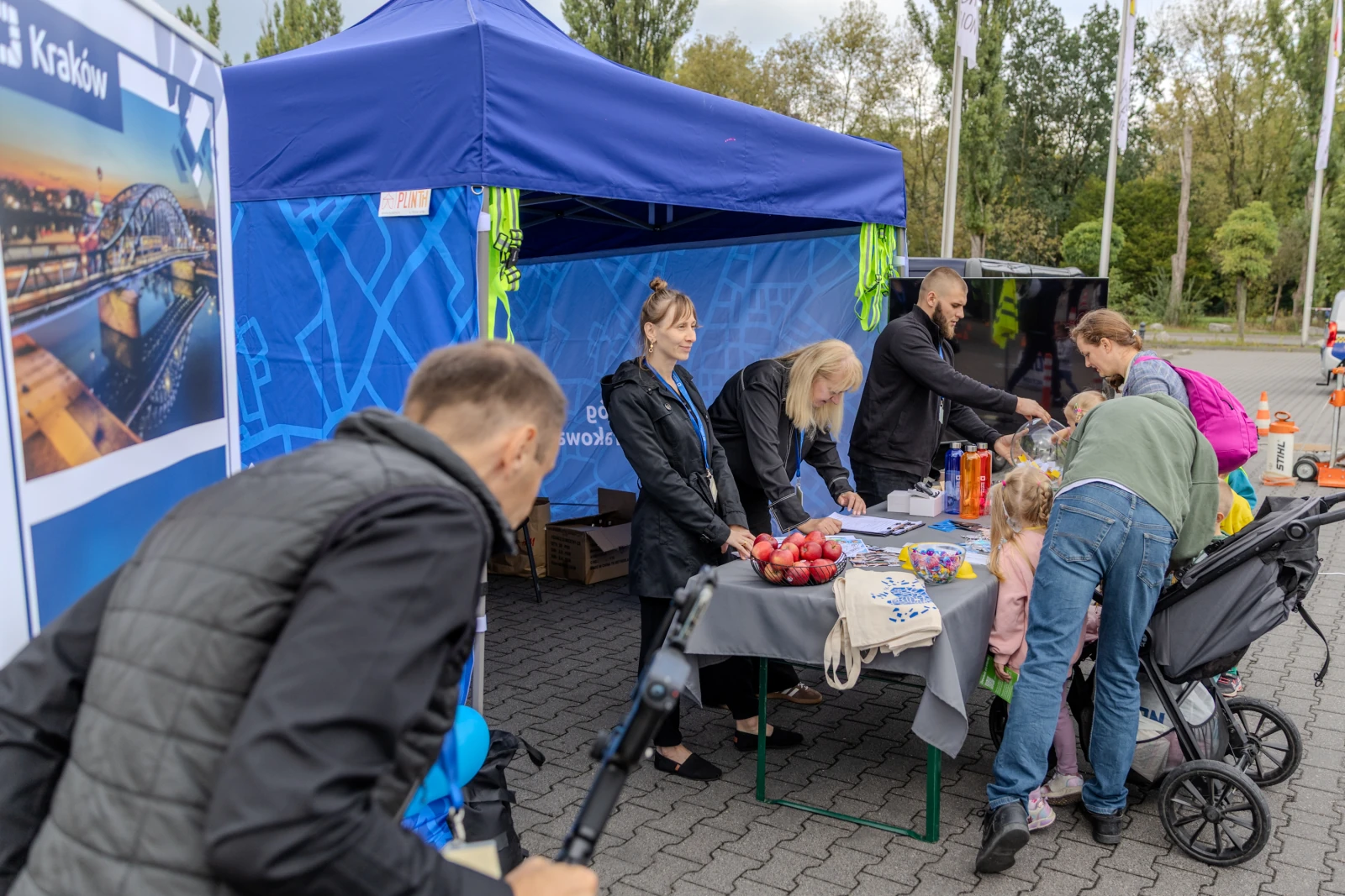 Stoiska informacyjne z ludźmi, dziećmi i owocami w plenerze.  Autor: Bogusław Świerzowski
