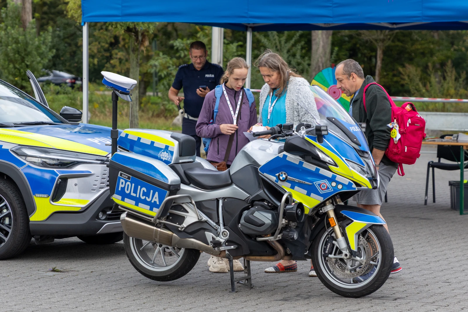Dwie osoby oglądają motocykl policyjny obok radiowozu.  Autor: Bogusław Świerzowski