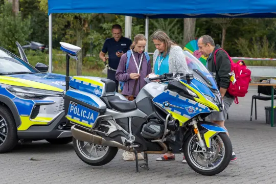 Dwie osoby oglądają motocykl policyjny obok radiowozu.