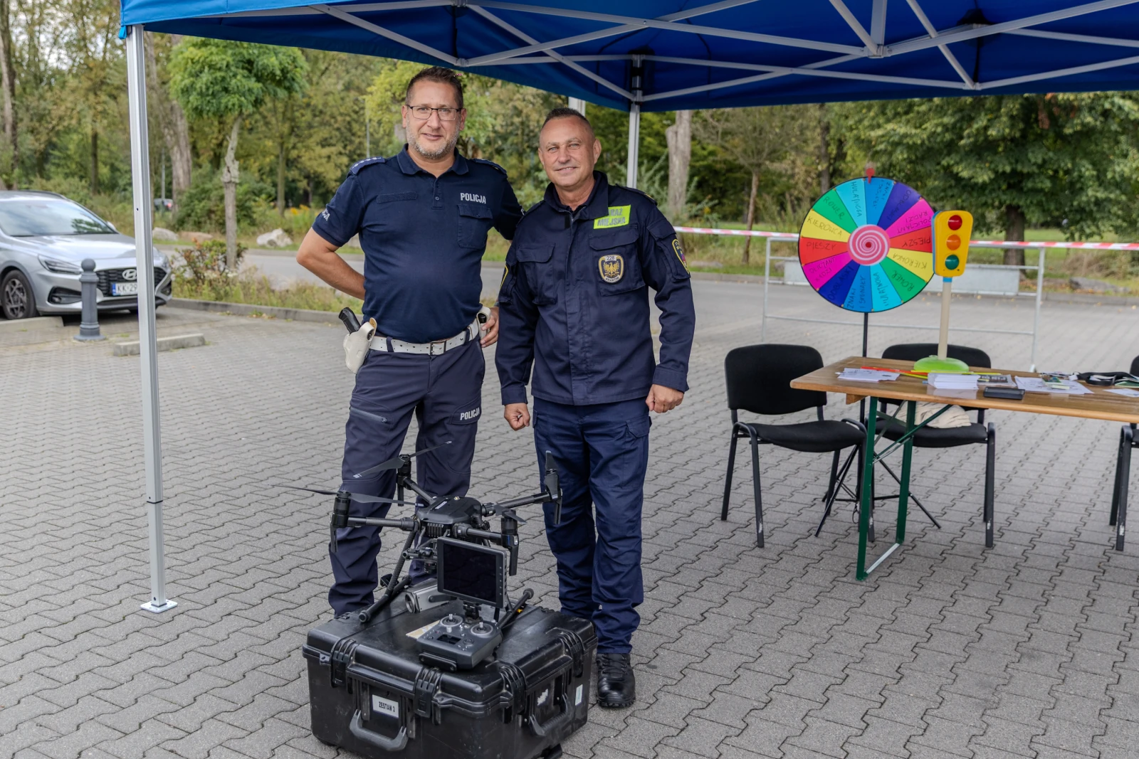Dwaj policjanci stoją obok drona i stoiska z kołem fortuny.  Autor: Bogusław Świerzowski