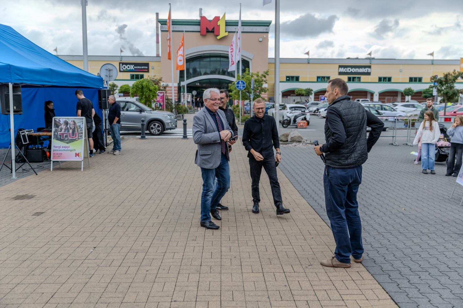 Trzech mężczyzn rozmawia przed centrum handlowym M1. W tle widoczny McDonald's.  Autor: Bogusław Świerzowski