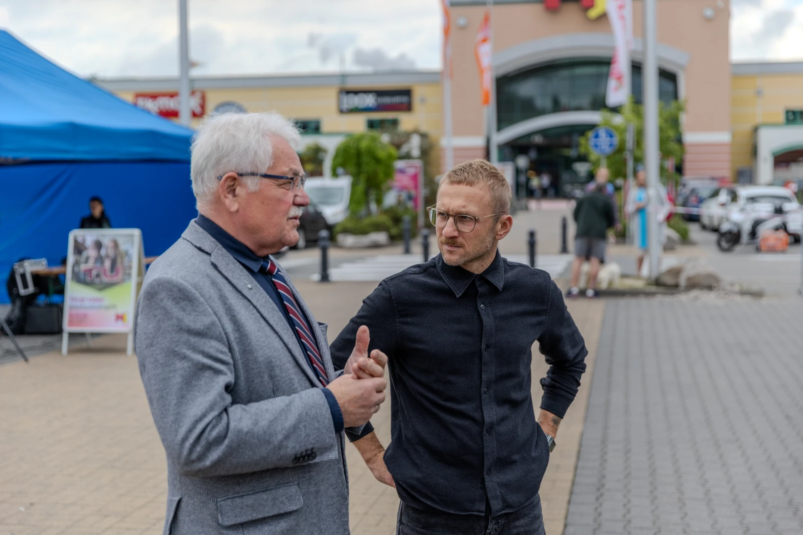 Dwóch mężczyzn rozmawia na tle centrum handlowego.  Autor: Bogusław Świerzowski