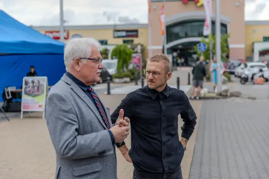 Dwóch mężczyzn rozmawia na tle centrum handlowego.