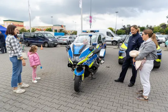 Motocykle policyjne z funkcjonariuszami i dziećmi w otoczeniu samochodów na parkingu.
