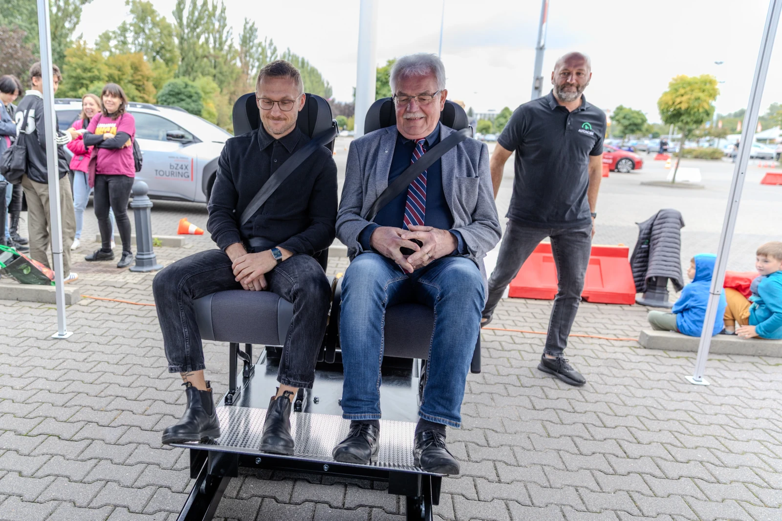 Mężczyźni siedzą na symulatorze, obok stoi inny mężczyzna, w tle grupa ludzi.  Autor: Bogusław Świerzowski