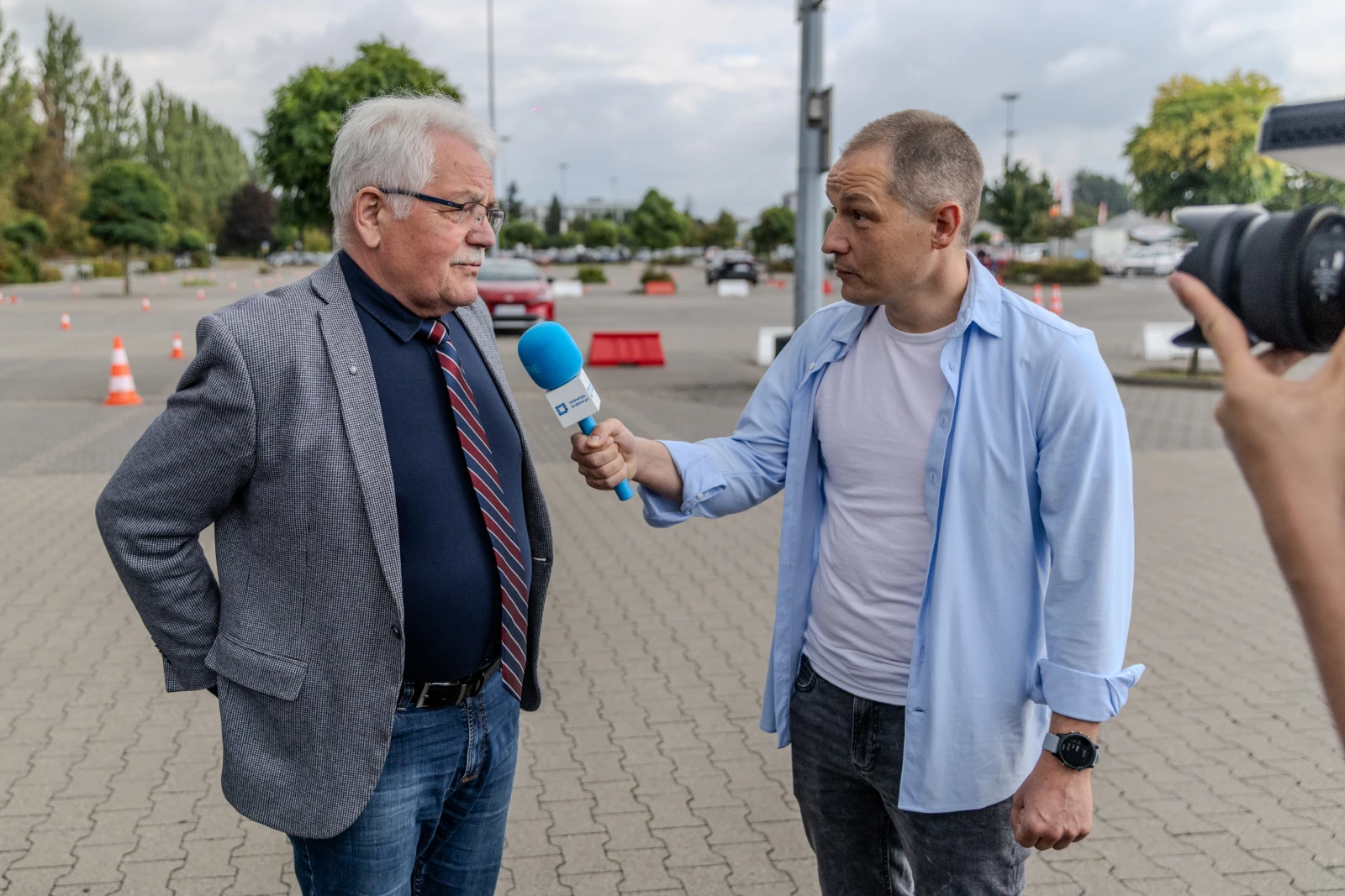 Dwóch mężczyzn rozmawia, jeden z mikrofonem, w tle plac z pachołkami.  Autor: Bogusław Świerzowski