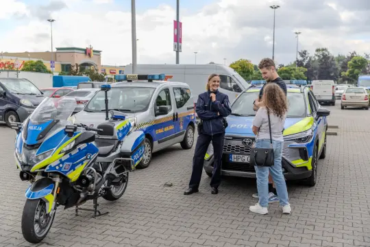 Policjanci rozmawiają z młodym mężczyzną i kobietą obok radiowozów i motocykla policyjnego.