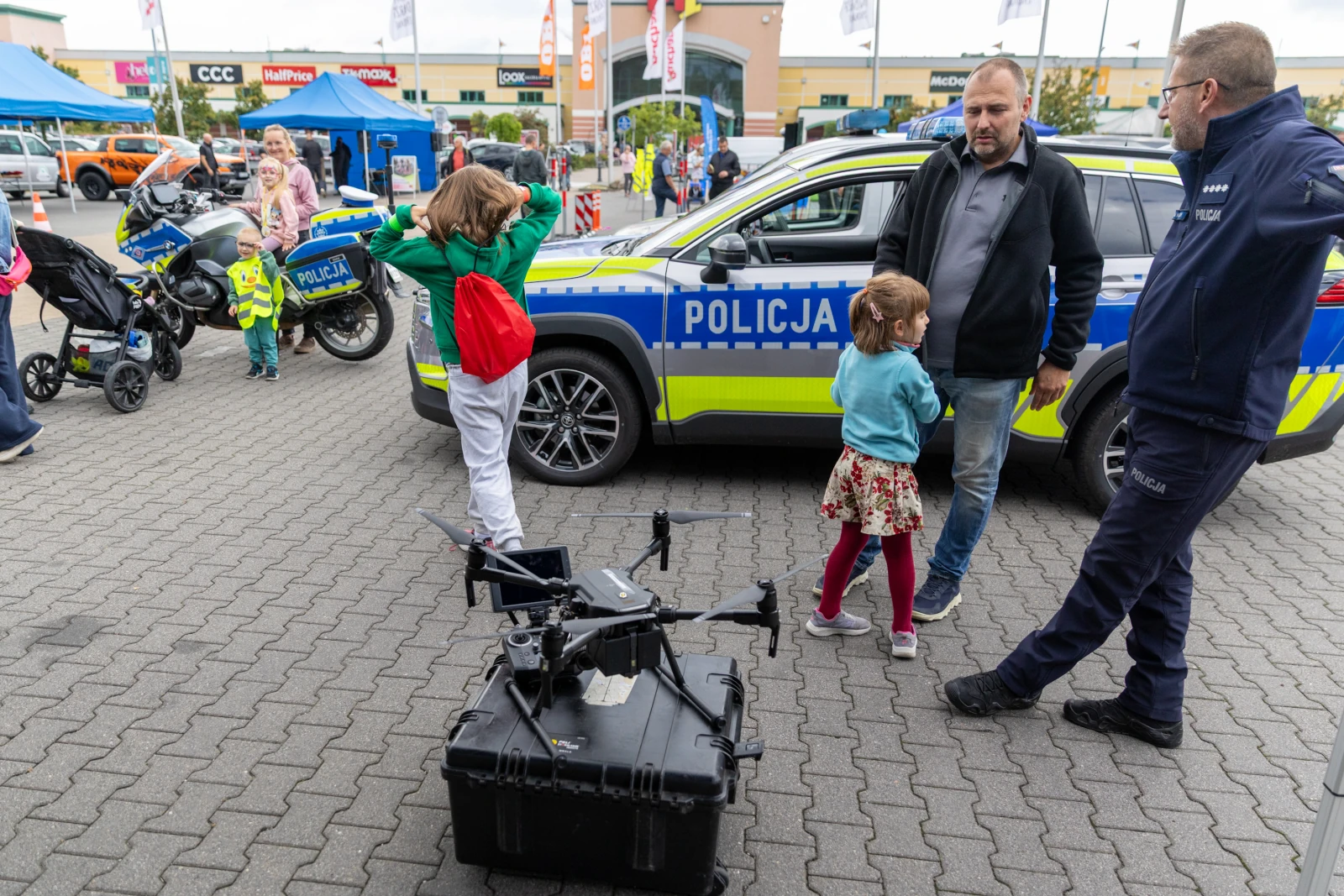 Dzieci bawią się w pobliżu policyjnego samochodu i drona.  Autor: Bogusław Świerzowski