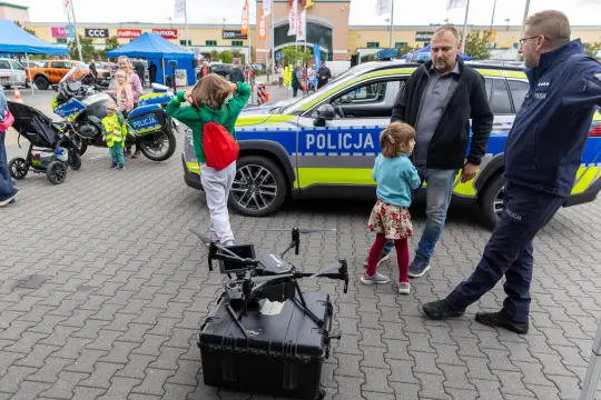 Dzieci bawią się w pobliżu policyjnego samochodu i drona.