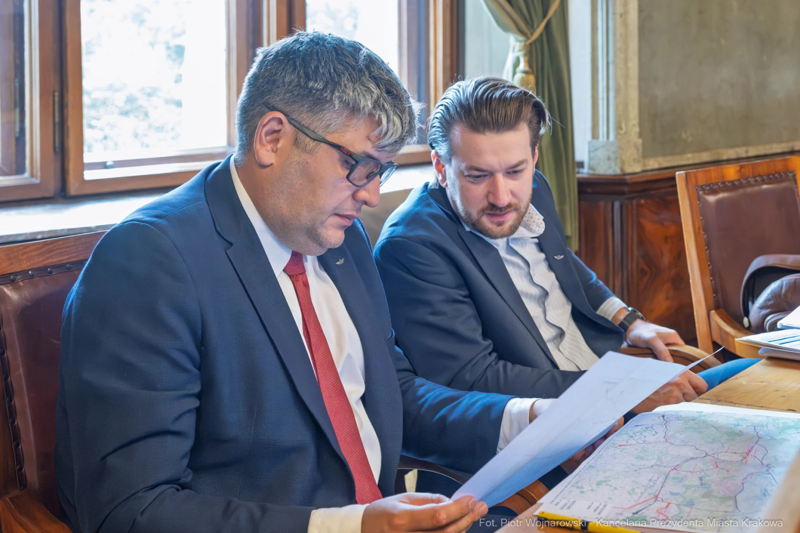 Dwóch mężczyzn w garniturach przegląda dokumenty przy stole w biurze.  Autor: Piotr Wojnarowski