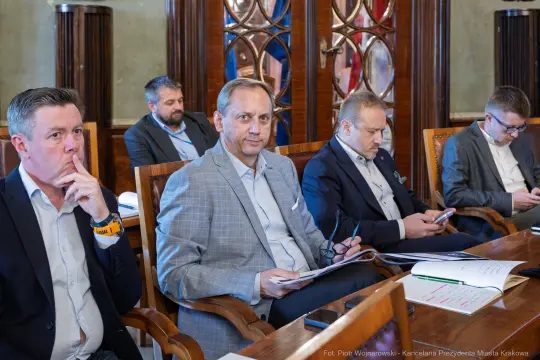 Grupa mężczyzn w garniturach siedzących przy stole, uczestniczących w spotkaniu.