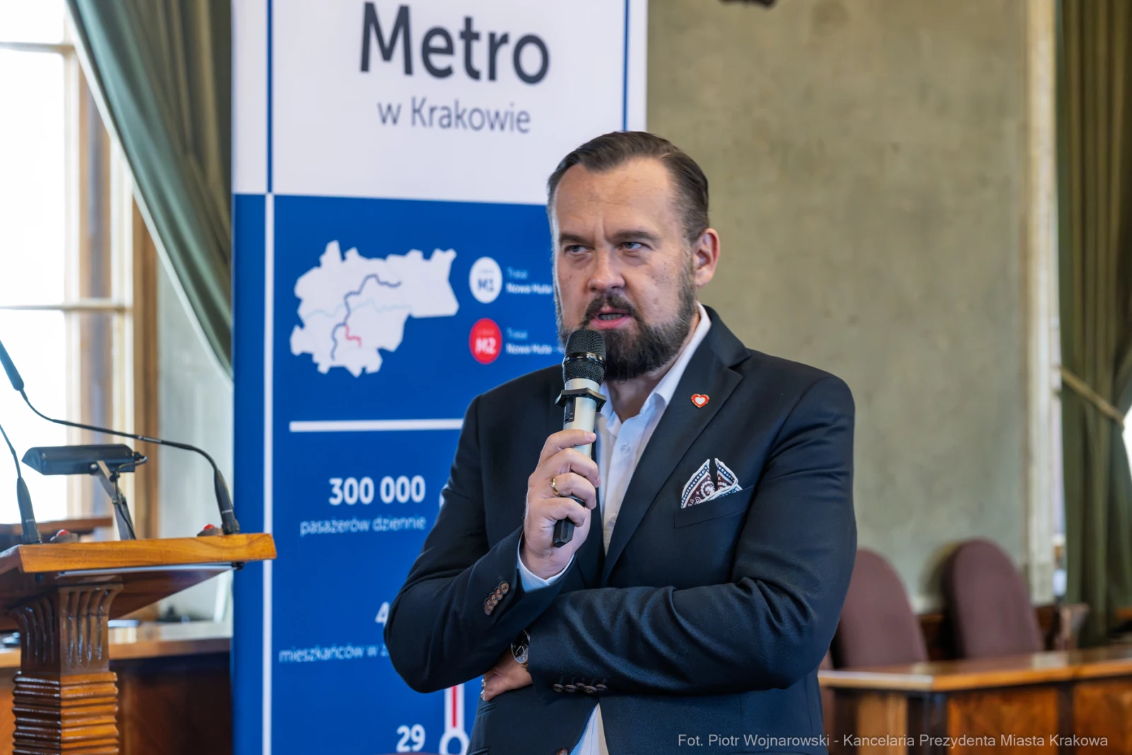 Mężczyzna z mikrofonem przemawia na tle plakatu dotyczącego metra w Krakowie.  Autor: Piotr Wojnarowski