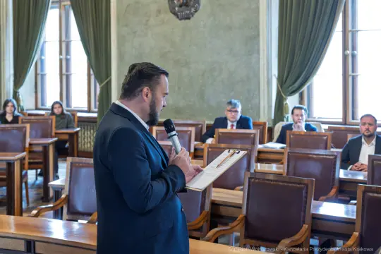 Mężczyzna w garniturze przemawia do zgromadzenia w sali obrad.