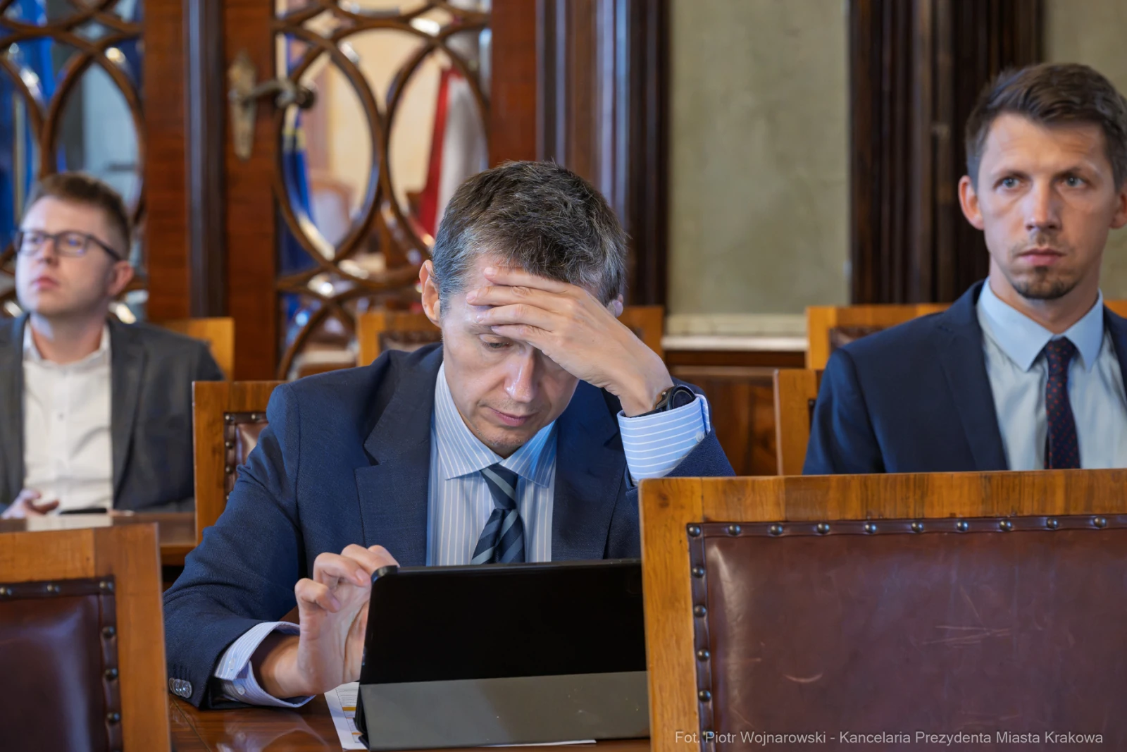 Mężczyzna w garniturze z tabletem, z wyraźnym zmartwieniem na twarzy, w sali obrad.  Autor: Piotr Wojnarowski