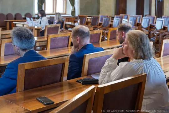 Grupa osób siedzących przy długim stole w sali konferencyjnej.