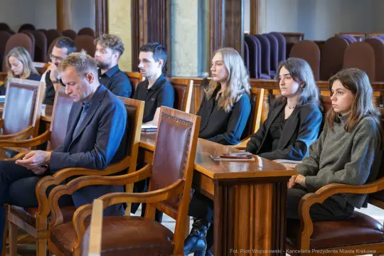 Grupa ludzi siedzących w sali obrad, skupionych na dyskusji.