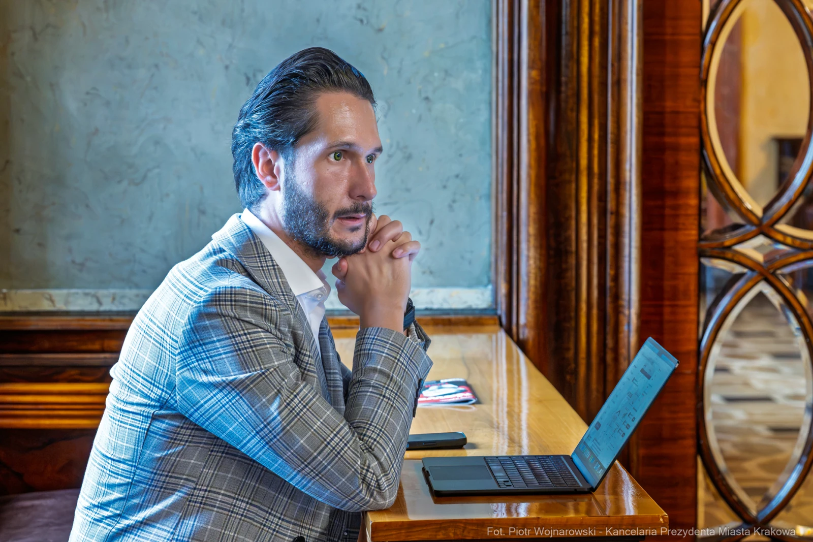 Mężczyzna w garniturze siedzi przy biurku z laptopem, zamyślony.  Autor: Piotr Wojnarowski