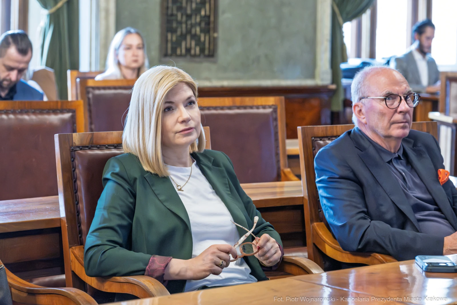 Kobieta w zielonej marynarce siedzi obok mężczyzny w okularach, oboje w sali obrad.  Autor: Piotr Wojnarowski