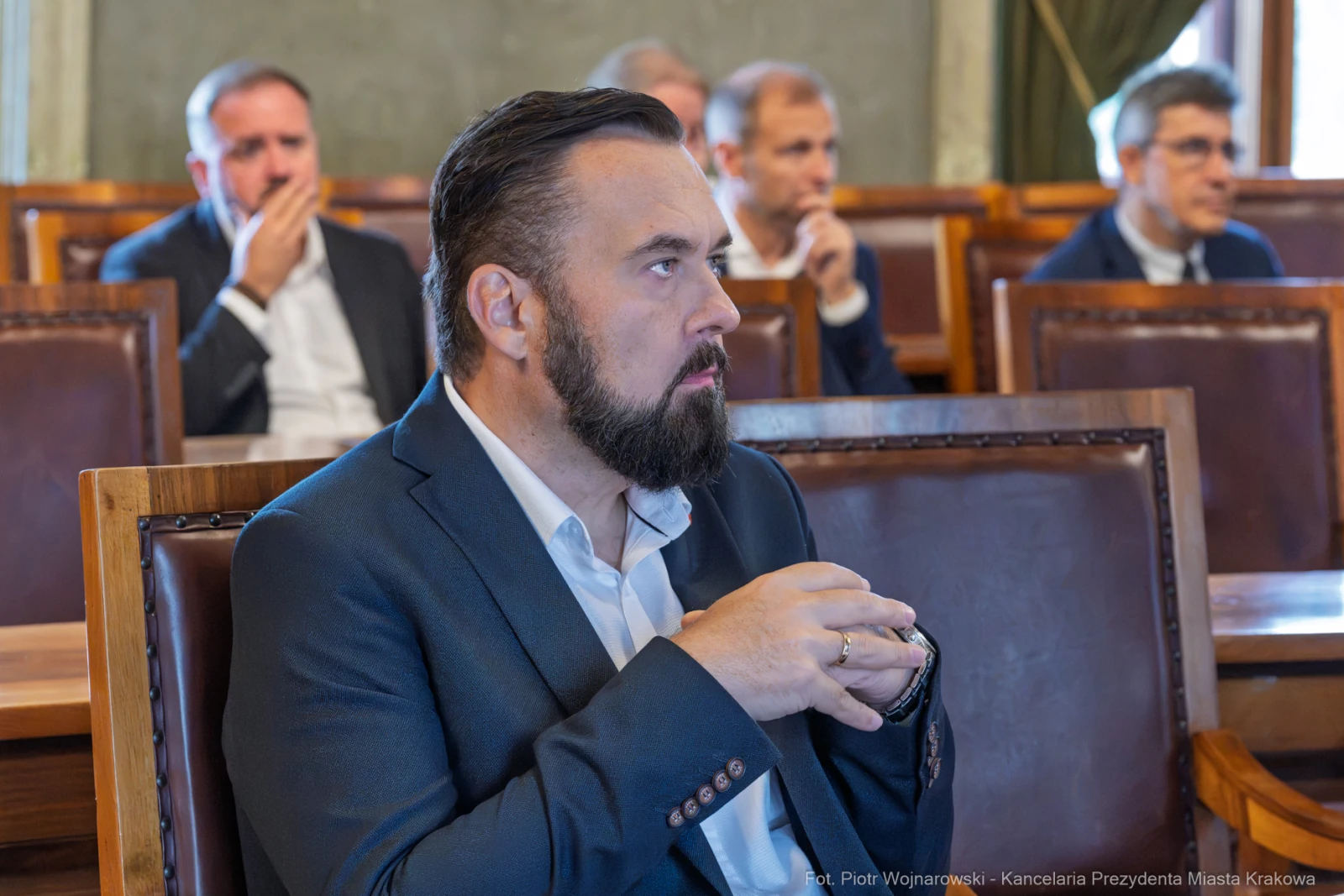 Mężczyzna w garniturze z brodą, siedzący w sali obrad, z zamyśloną miną.  Autor: Piotr Wojnarowski
