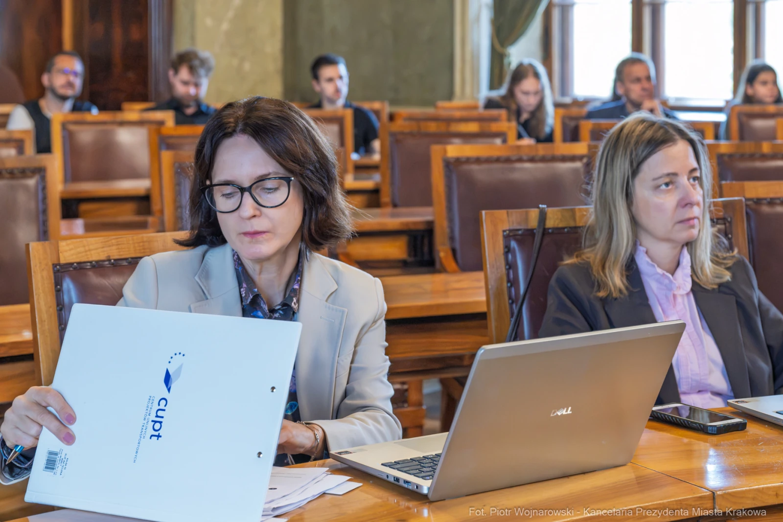 Kobiety siedzące przy stole, jedna z dokumentami, druga z laptopem, w tle uczestnicy spotkania.  Autor: Piotr Wojnarowski