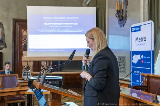 Kobieta przemawia na konferencji, w tle prezentacja dotycząca geologii i metra w Krakowie.