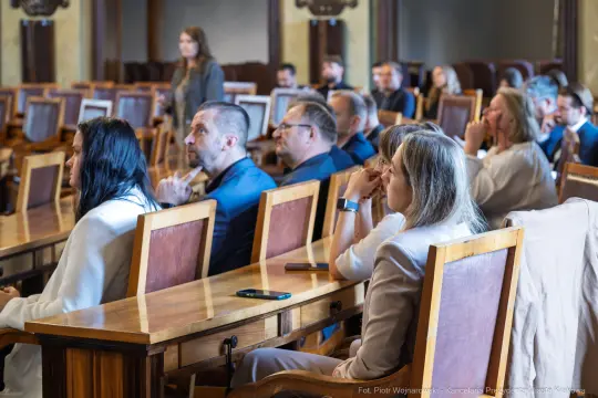 Grupa osób siedzących w sali obrad, skupionych na prezentacji lub dyskusji.