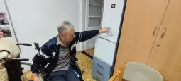 Mężczyzna na wózku inwalidzkim wskazuje na lodówkę.